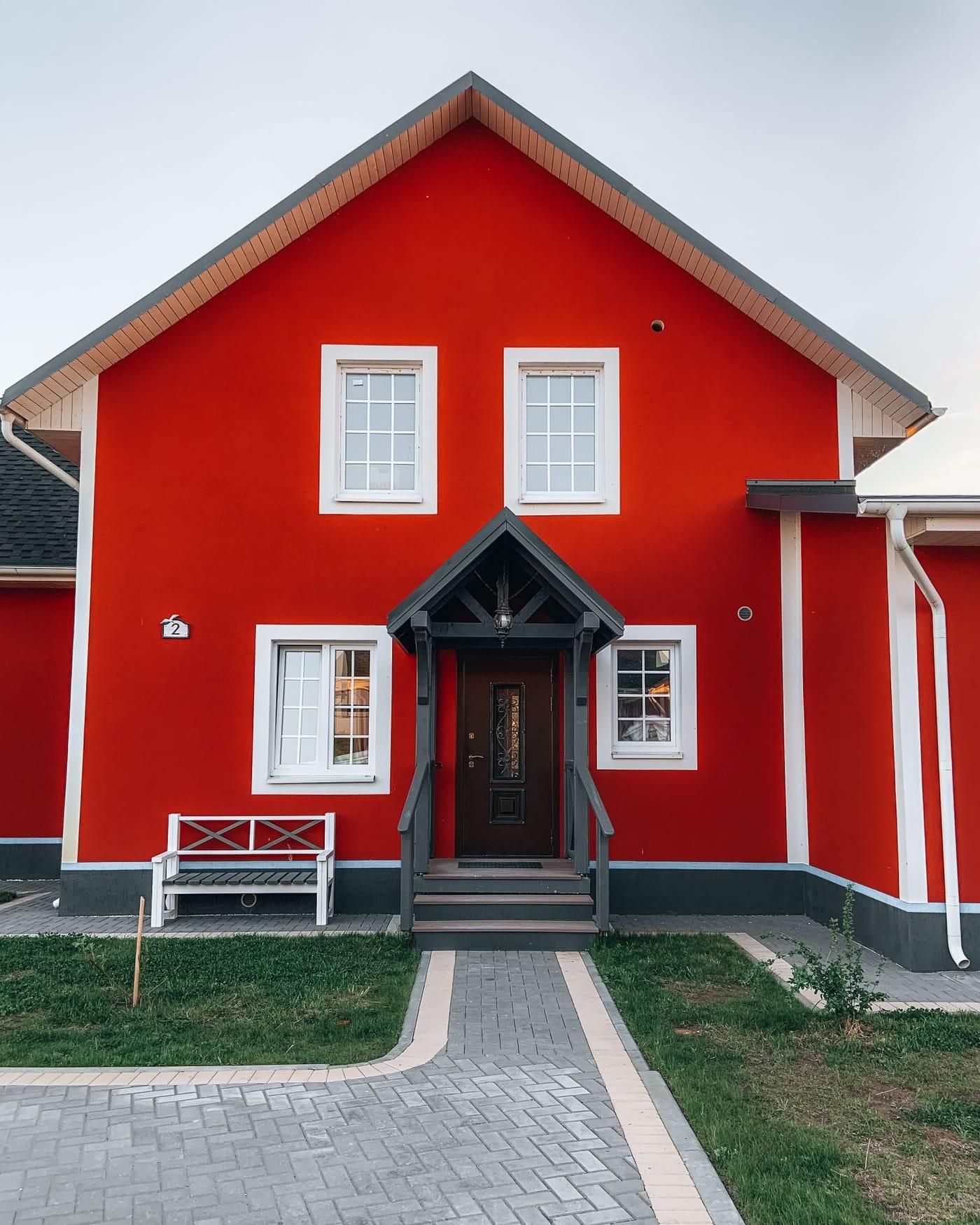 Façade de maison fraîchement repeinte en rouge vif, encadrements de fenêtres blancs